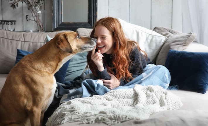 Young woman and dog laughing on couch